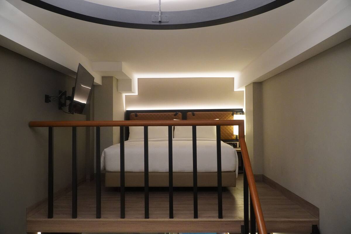 Une chambre à coucher avec un lit, un téléviseur fixé au mur et un escalier menant à l’étage supérieur.