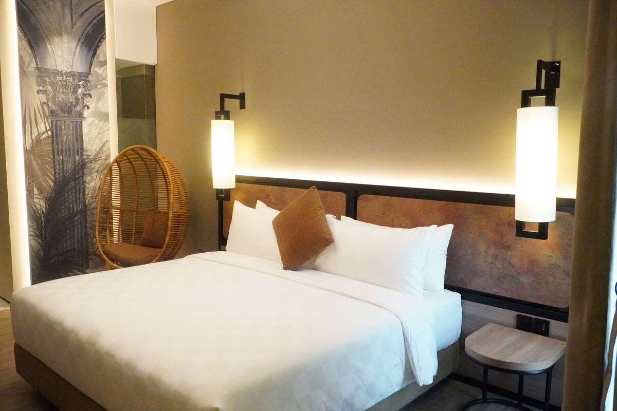 Un lit bien fait, avec du linge de lit blanc, un oreiller marron et deux lampes fixées au mur.