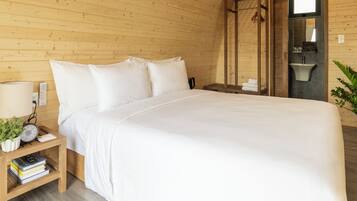 Una habitación de madera con cama, mesita de noche y un pequeño baño.