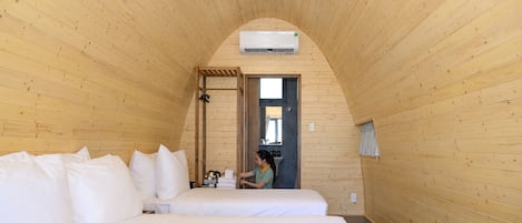 Habitación con paneles de madera, una cama, una mesita y un equipo de aire acondicionado.