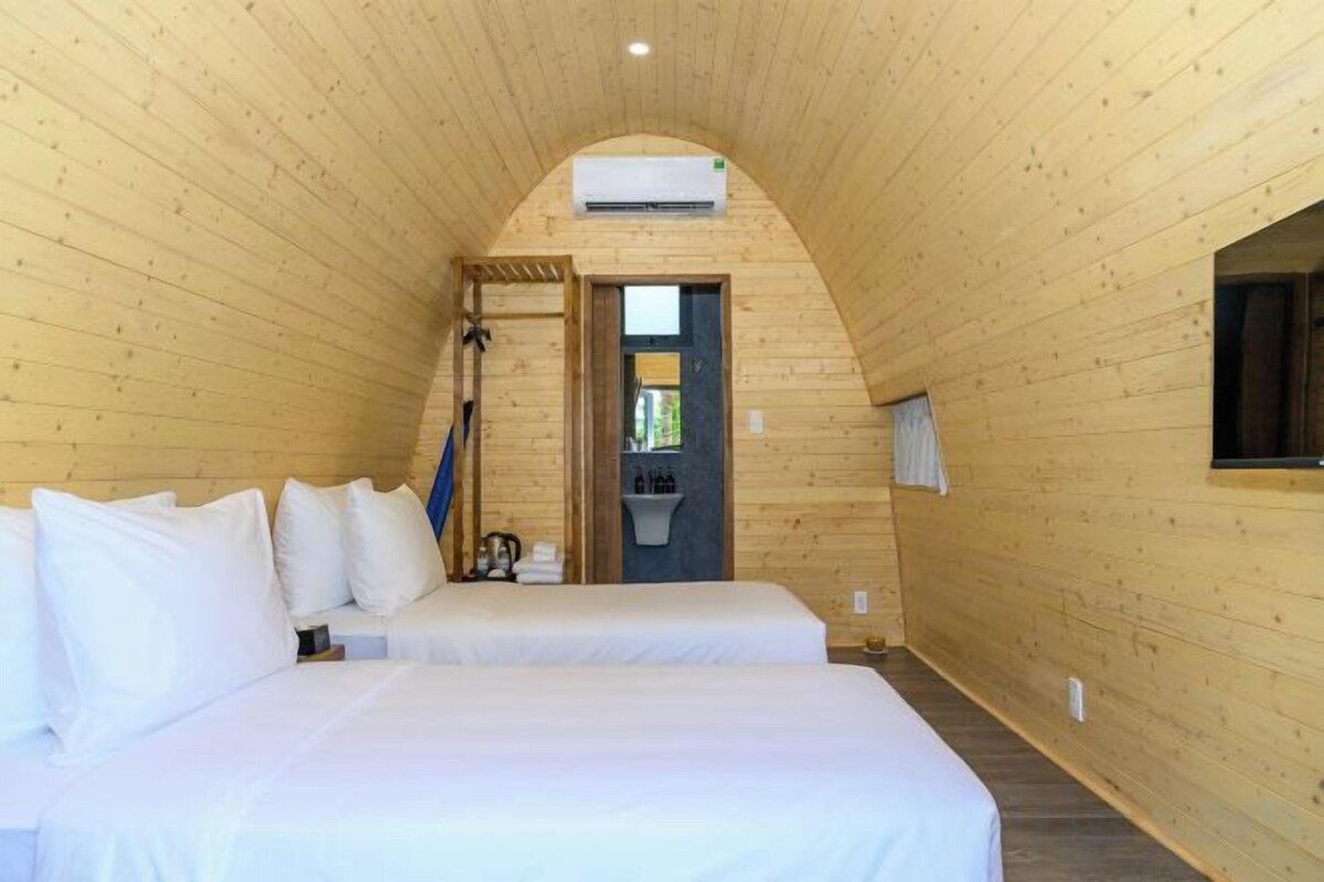 Un dormitorio de cabaña de madera con dos camas, una ventana y una puerta que da a un baño.