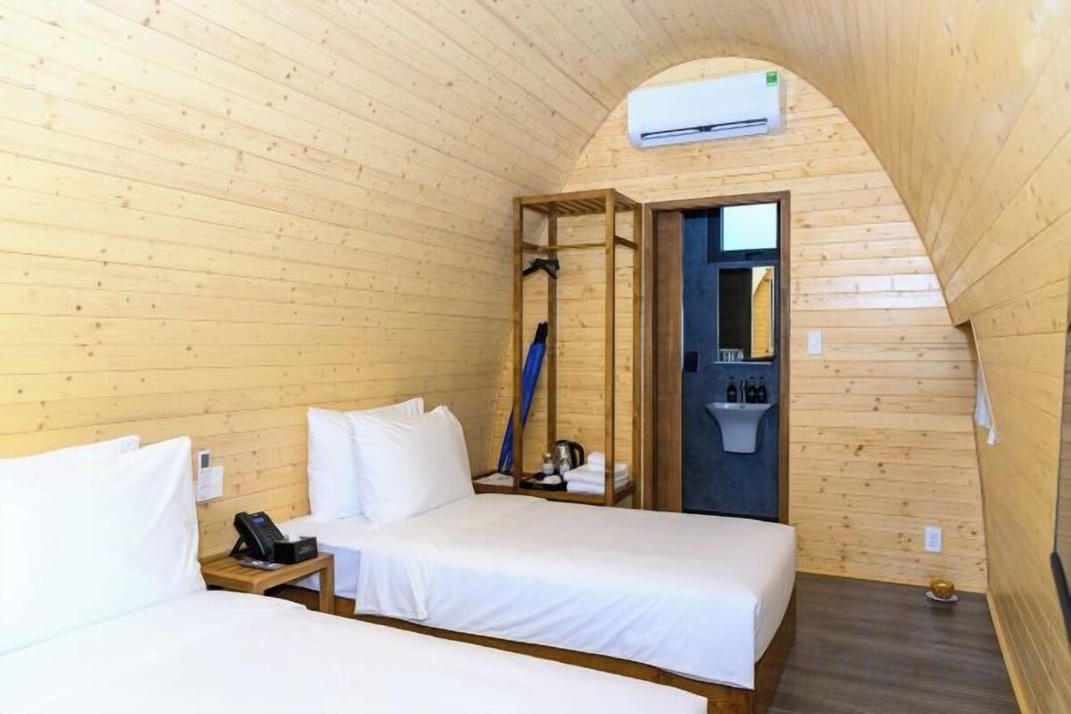 Una habitación pequeña de madera con dos camas, una zona de ducha y un equipo de aire acondicionado a la vista.