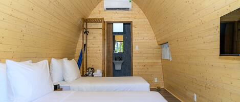 Acogedora habitación tipo cabaña de madera con dos camas, un lavamanos pequeño y una ventana.