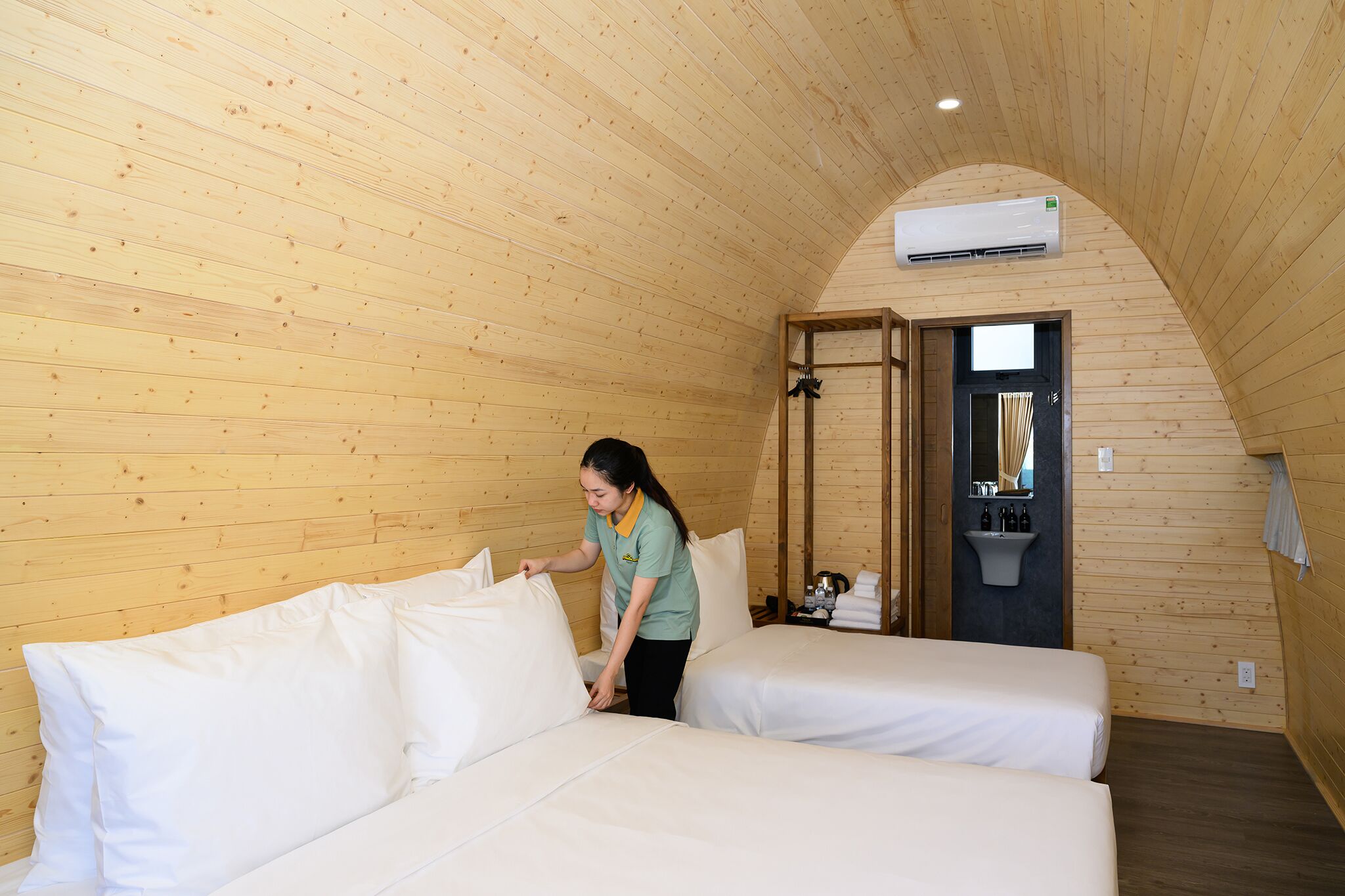 A wooden-paneled room with two beds, a sink, and an air conditioning unit.