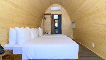 Um quarto de madeira com uma cama, uma mesinha e uma porta para o banheiro.