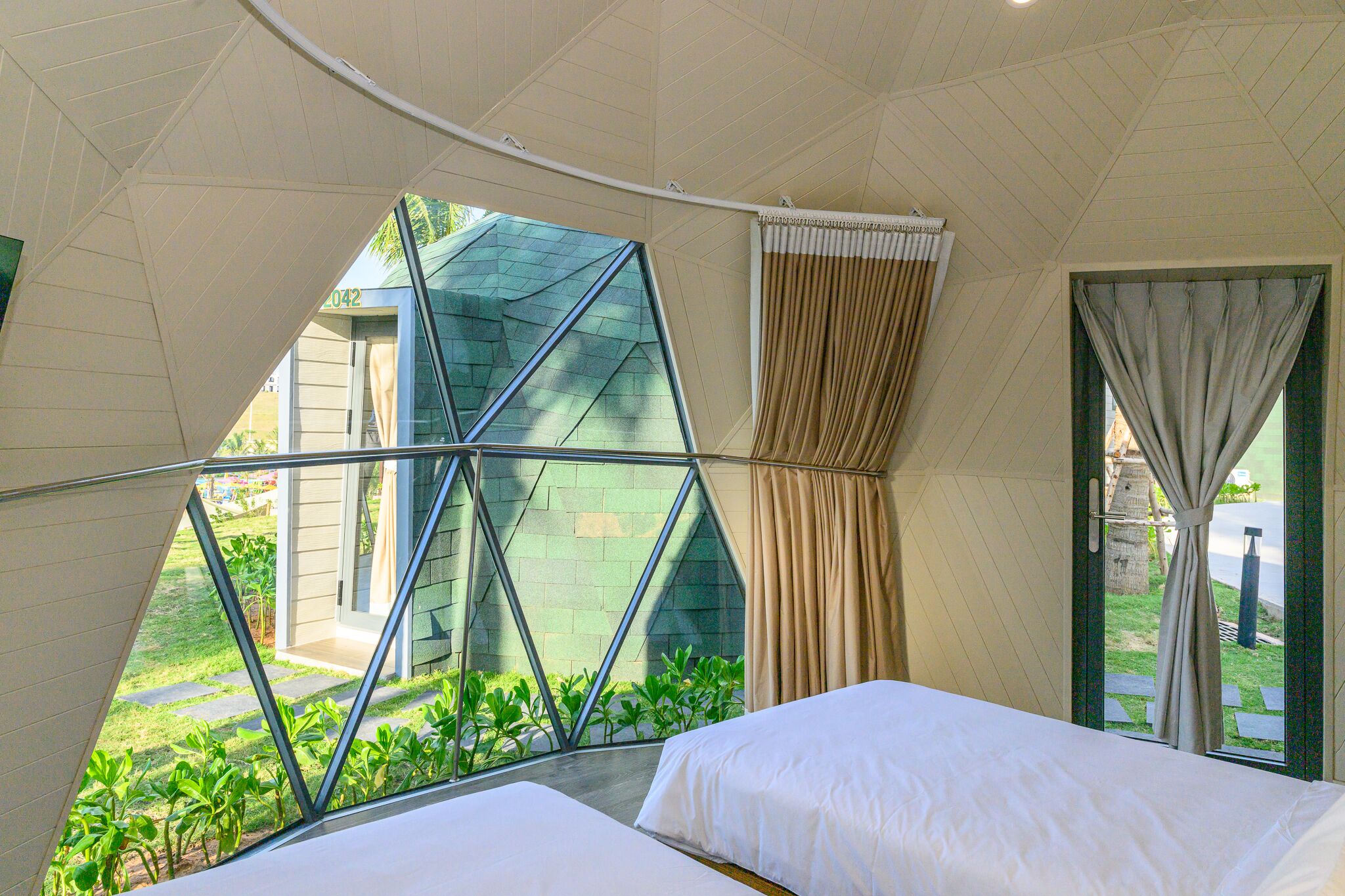 A modern hotel room with a large window, a bed, and a view of the garden.