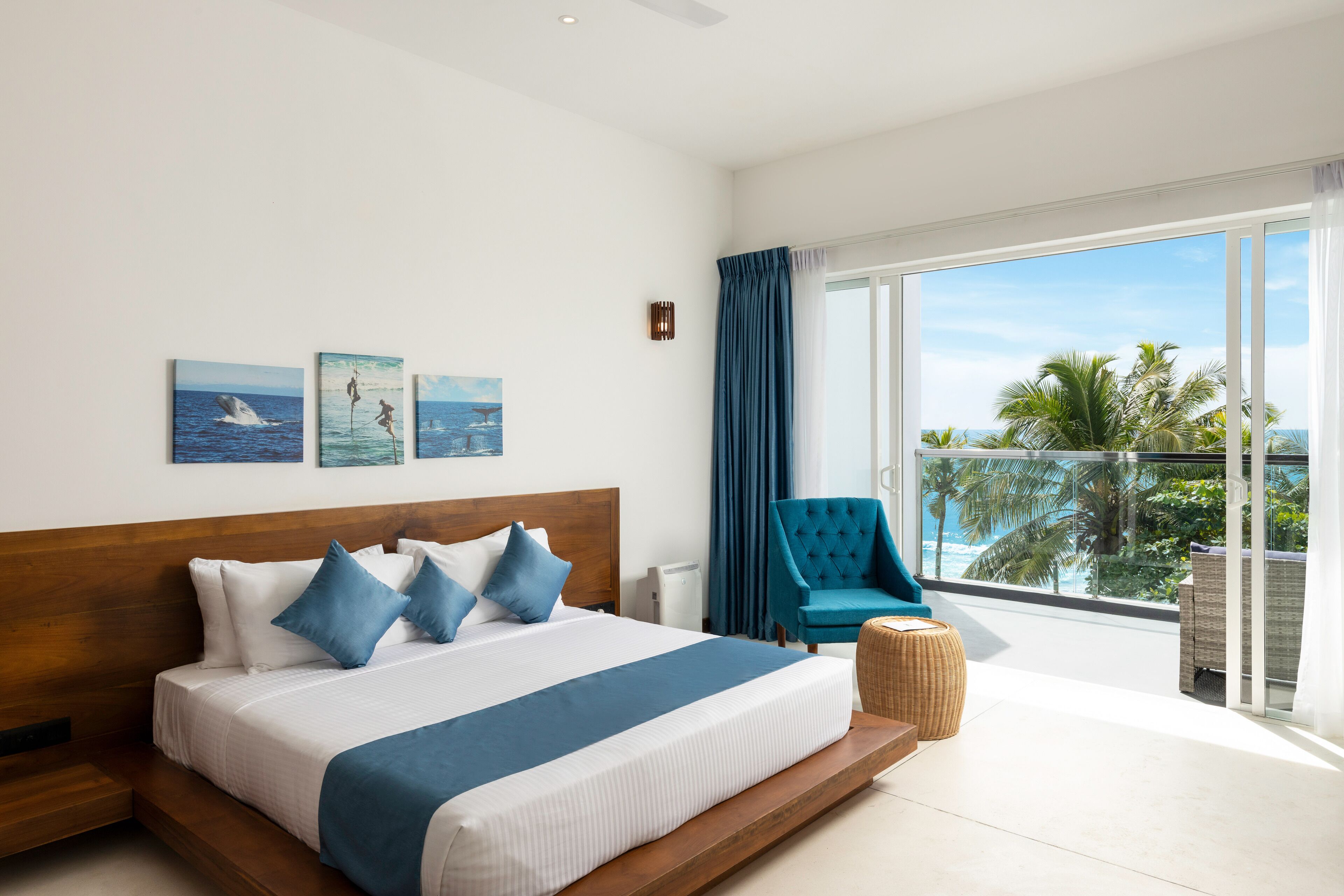 Una camera d'albergo moderna con un grande letto, vista sull'oceano e un balcone con palme.