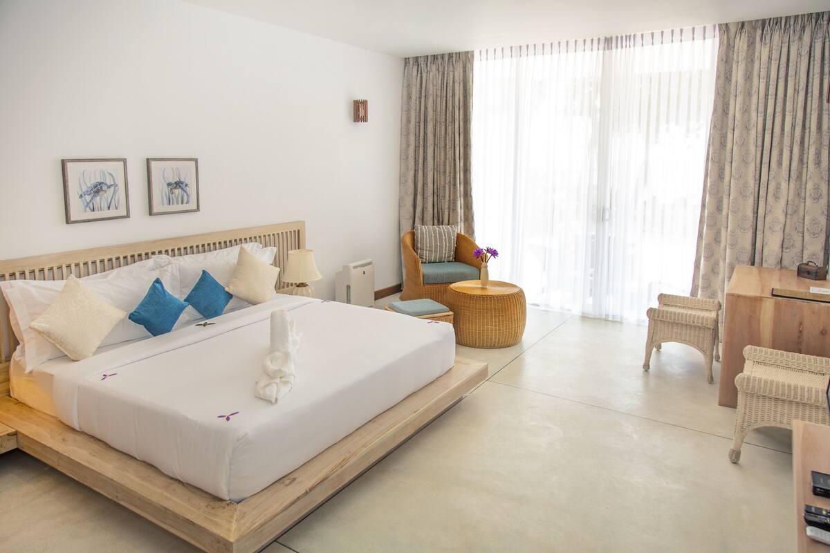 A hotel room with a large bed, a desk, wicker furniture, and artwork on the wall.