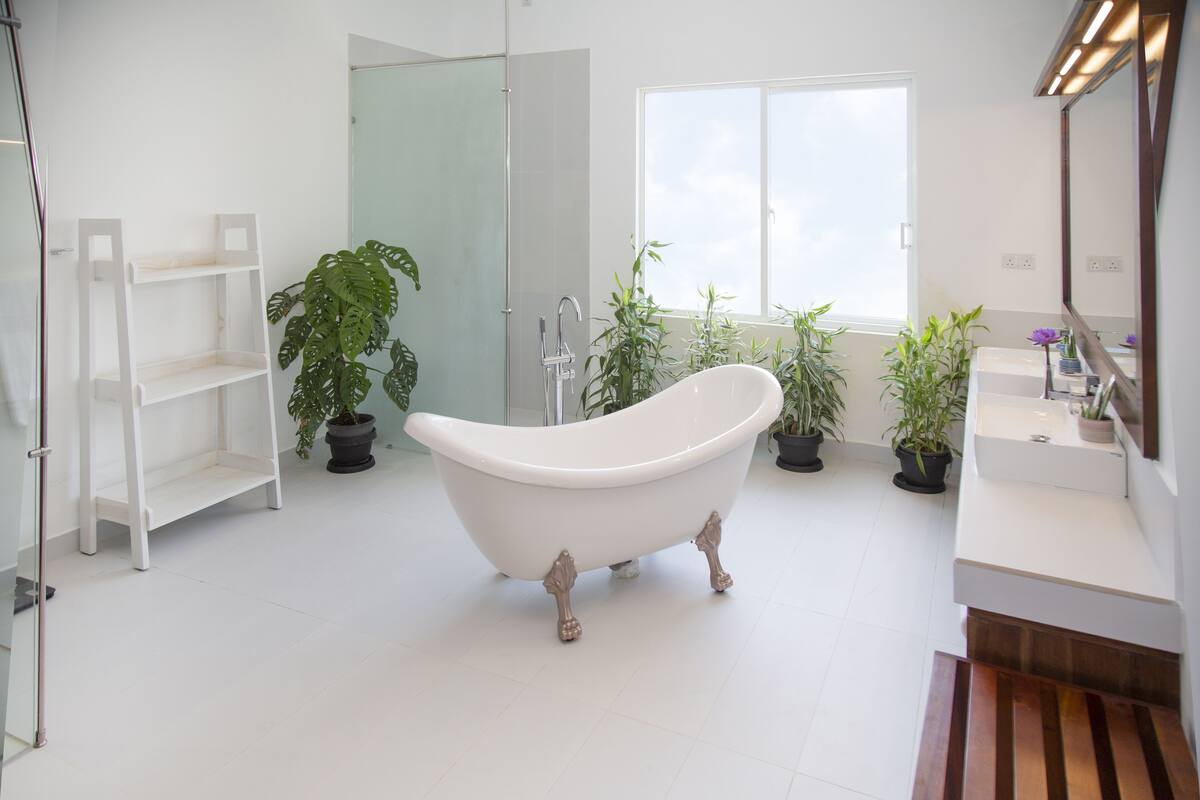 A modern bathroom with a freestanding bathtub, white shelves, and potted plants.