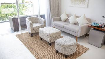 En moderne stue med sofa, to lænestole, skodder, et sofabord og et lille køleskab.