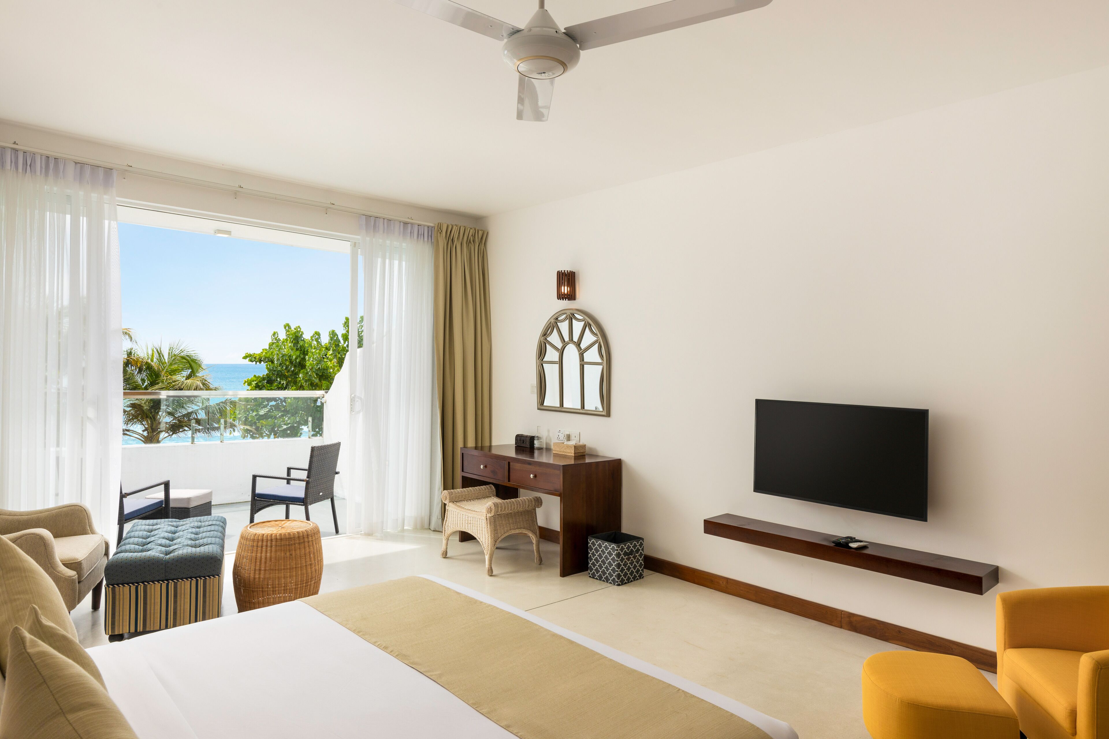 A hotel room with a bed, a desk, a television, and a balcony with a view of the sea.
