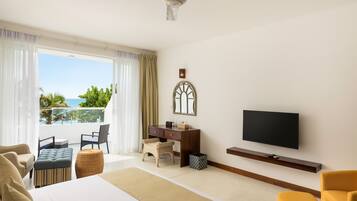 A hotel room with a bed, a desk, a television, and a balcony with a view of the sea.