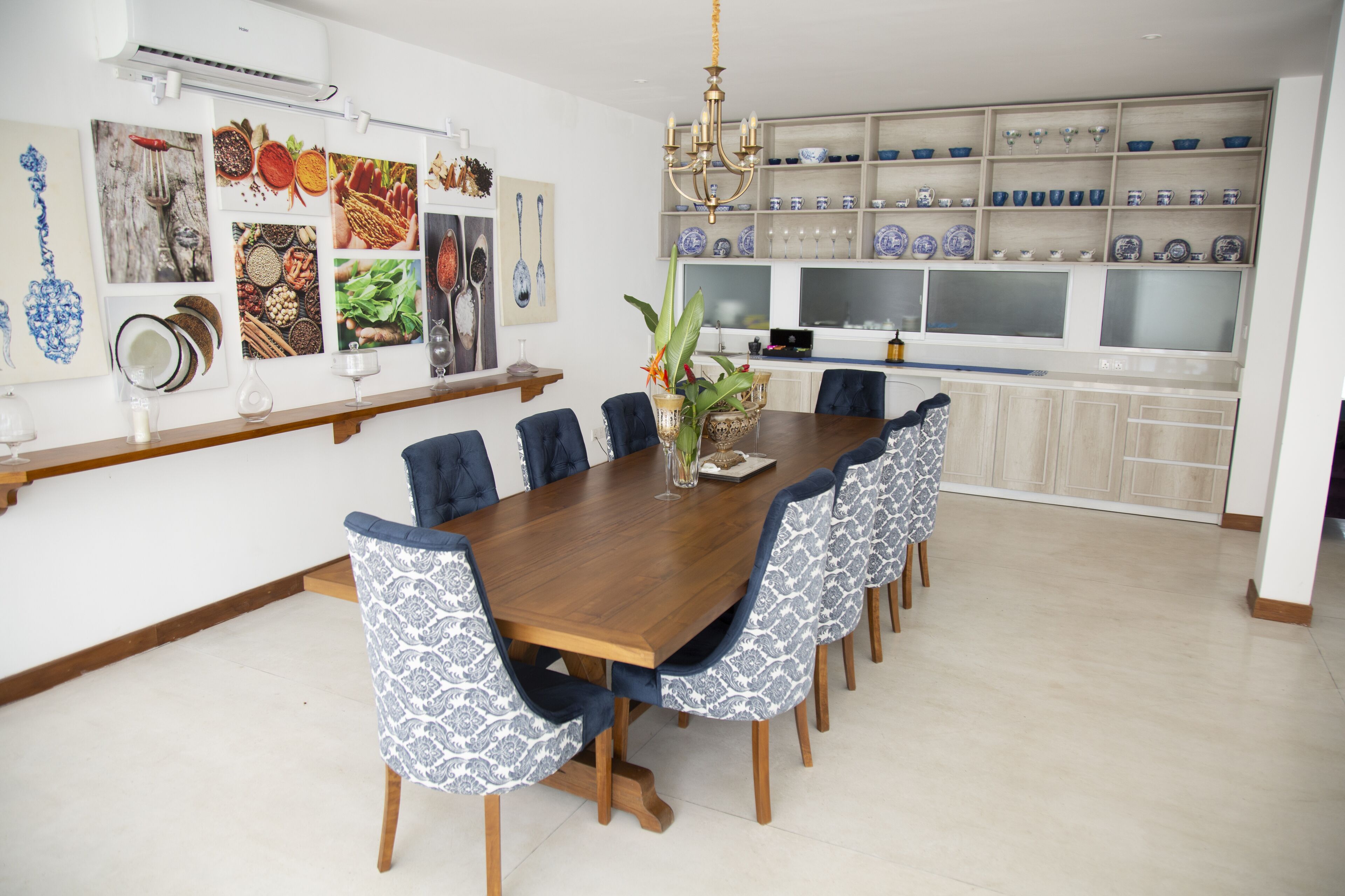 Un coin repas avec une table en bois et des chaises à motifs, un lustre et un mur orné d’assiettes décoratives et d’œuvres d’art.
