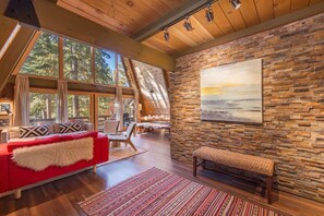 Uma sala de estar ampla, com um sofá vermelho, piso de madeira e uma parede de pedra com um quadro.
