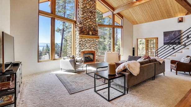 A spacious living room with large windows, a stone fireplace, and a staircase. - Modern, Hot Tub, Lake View, Short Drive to Beach, Restaurants, and Shops- Flying Flamingo (Kings Beach)