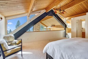 Una camera da letto con un letto grande, una sedia con una coperta in pelliccia bianca, un soffitto a falde con travi in legno e vista sull'esterno attraverso una finestra.