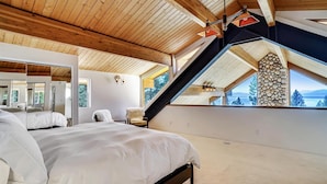 A bedroom with a large bed, a wooden ceiling, and a stone wall. - Modern, Hot Tub, Lake View, Short Drive to Beach, Restaurants, and Shops- Flying Flamingo (Kings Beach)