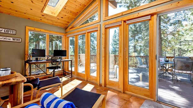 Een gezellig cabin interieur met een houten plafond, grote ramen, een televisie en een eethoek.