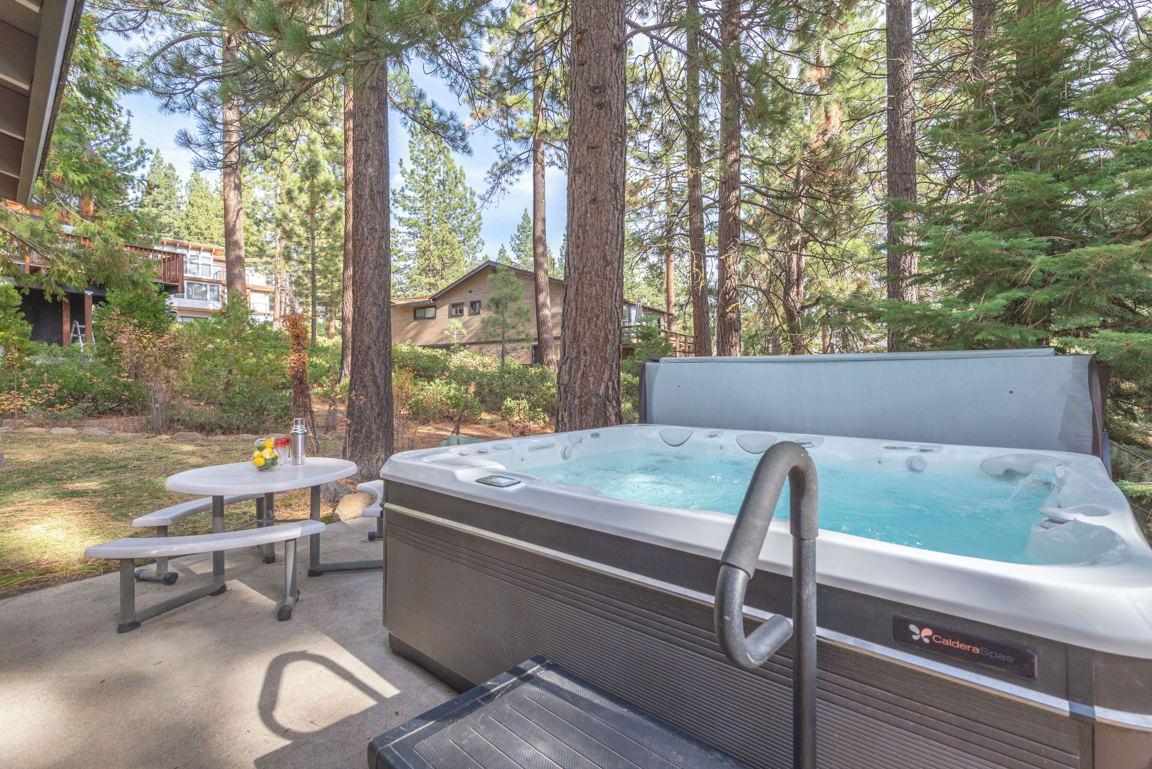 Jacuzzi con escalera, mesa de picnic y banco en zona boscosa con árboles altos.