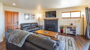 A living room with a leather sofa, a coffee table, a fireplace, a television, and a window with blinds. - Sandy yard that backs to the Beach! Walk to town -Lakefront on the Beach (Kings Beach)