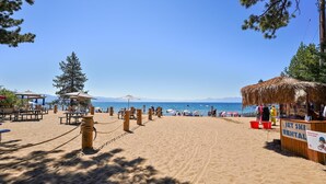 A beach with wooden benches and umbrellas, a thatched-roof structure, and a sign indicating a rental shop. - Sandy yard that backs to the Beach! Walk to town -Lakefront on the Beach (Kings Beach)