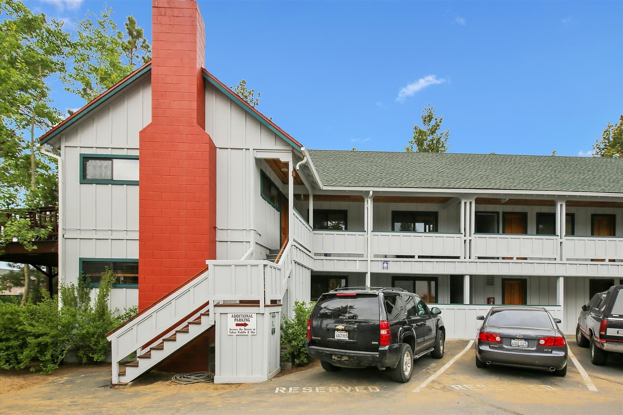 A two-story building with a red chimney, a covered porch, and a parking area with two cars.