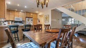 Une cuisine moderne avec des meubles en bois, une table à manger avec des chaises, un lustre et un escalier menant à un autre niveau.