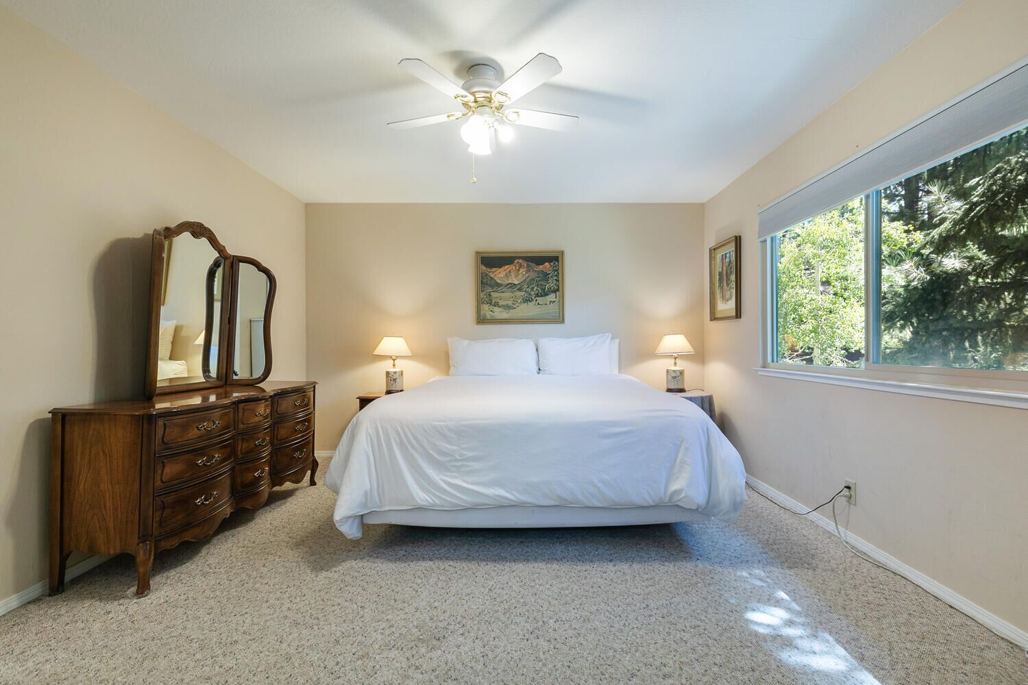 A bedroom with a bed, dresser, ceiling fan, and large windows.