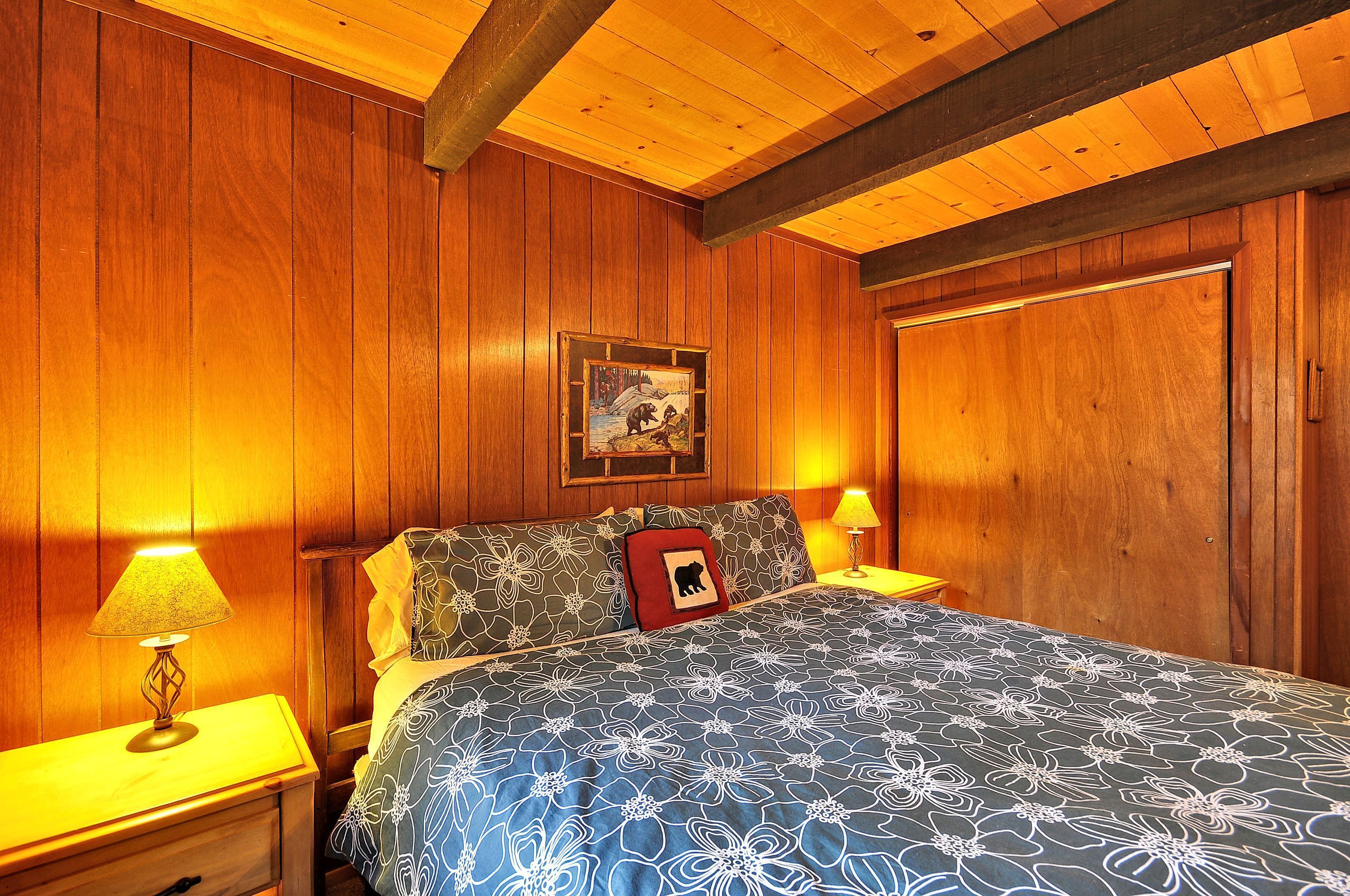 Ein Zimmer mit Holzwänden, einem Bett, zwei Nachttischlampen und einem gerahmten Bild an der Wand.