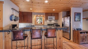 Una cocina con armarios de madera, un refrigerador de acero inoxidable y una barra con taburetes.