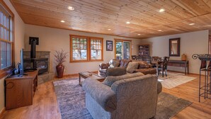 Una sala de estar acogedora con chimenea, sofá de cuero, piso de madera y ventanas amplias.