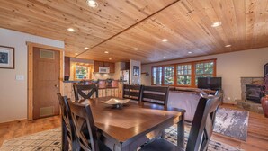 Comedor con paneles de madera, una mesa y sillas, una cocina al fondo y una chimenea.
