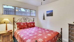 A bedroom with a bed, a wooden nightstand, a lamp, a dresser, a window, and a ceiling fan.