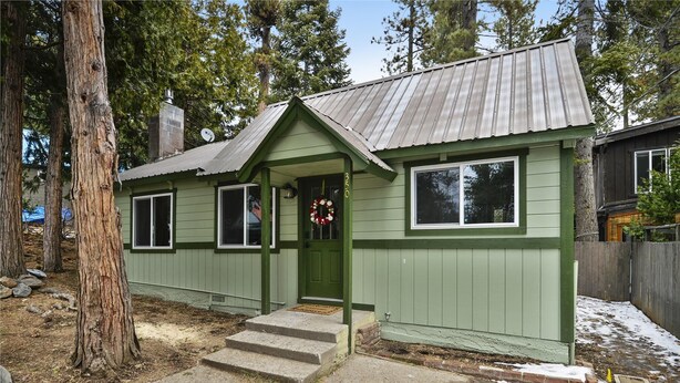 A small, single-story house with a green exterior, a metal roof, and a front porch with steps leading to the door.