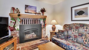 A cozy living room with a fireplace, a sofa, a TV, and a lamp.