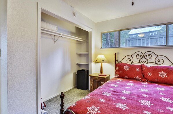 A bedroom with a bed, a nightstand, a lamp, a closet, and a window with a view of a house. - Walk to Beach Restaurants & Shops in Tahoe City- Dogs OK -Green Grove Cottage (Tahoe City)