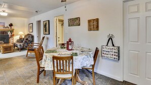 A dining room with a table set for four, surrounded by wooden chairs. A ceiling fan is visible above the table, and there are wall decorations including a 'Blessed' sign and a bicycle-themed piece.
