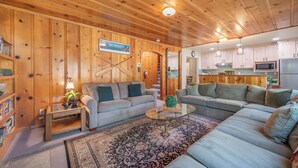A cozy living room with wooden walls and ceiling, a large sofa, a coffee table, and a bookshelf. - Walk to Beach and Town, Dogs OK, Cozy Fireplace, -Steelhead Mountain Retreat (Kings Beach)