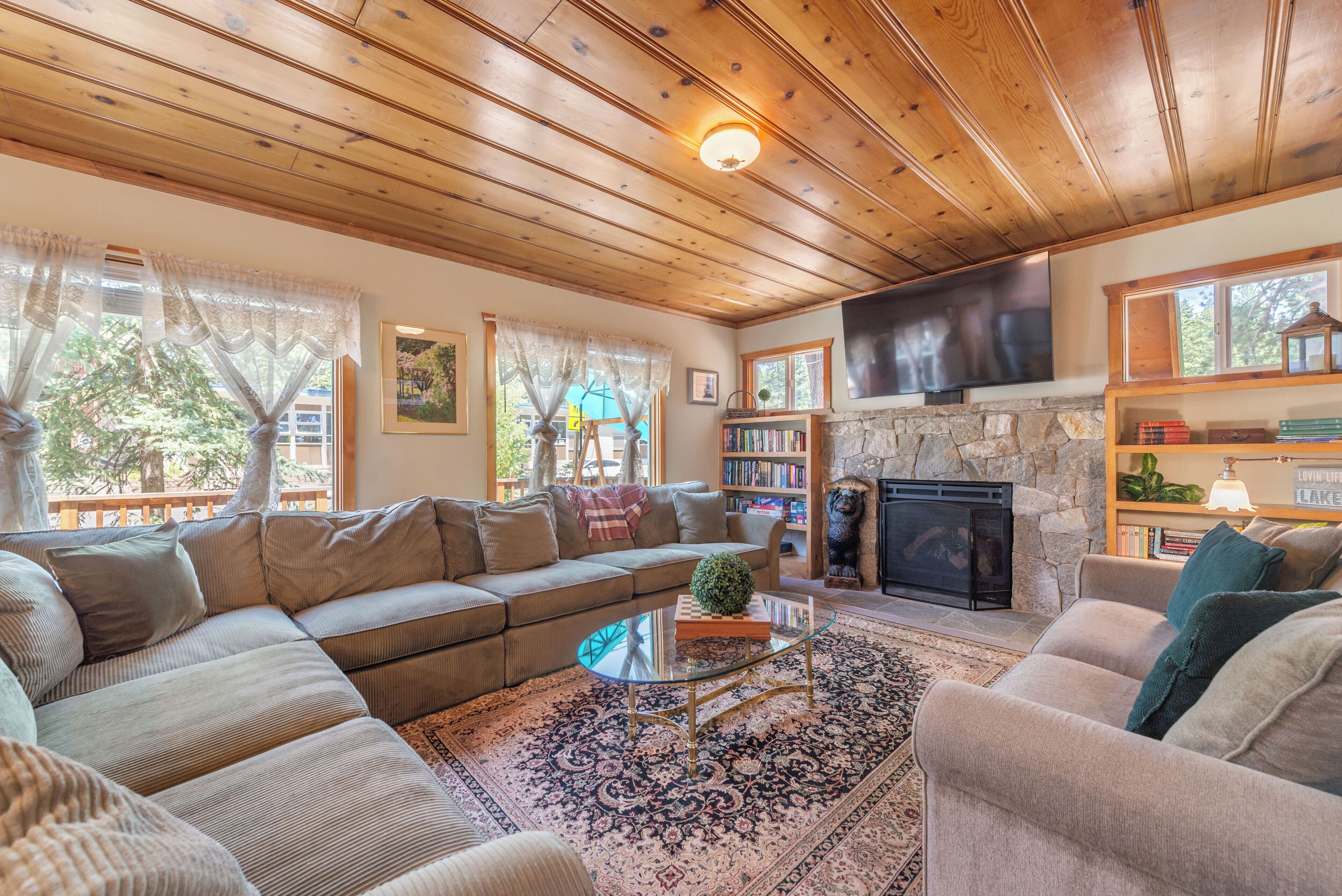 A cozy living room with a sectional sofa, a glass coffee table, a fireplace, and a bookshelf.