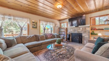 A cozy living room with a sectional sofa, a glass coffee table, a fireplace, and a bookshelf.
