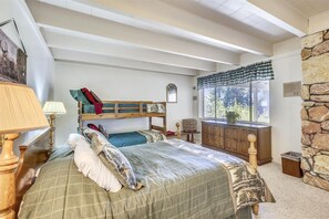 Une chambre avec un lit superposé, une grande fenêtre donnant sur les arbres, un mur en pierre et une armoire en bois.