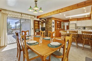 A dining area with a wooden table set for six, surrounded by chairs with green cushions. A stone pillar and wooden shelves are visible in the background. - Dollar Pointe of View- Hot Tub, Lake View, Close to Beach (Tahoe City)