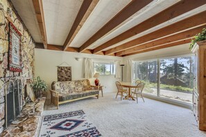 Une pièce chaleureuse avec une cheminée en pierre, un canapé à motifs, une table à manger avec des chaises et une grande fenêtre donnant sur l’extérieur.