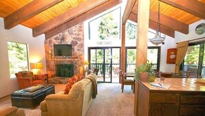 Ein gemütliches Wohnzimmer mit Kamin aus Stein, einem Flachbildfernseher und einem großen Fenster mit Blick auf eine Terrasse.