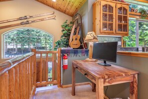 Una scrivania in legno con un computer, una finestra che si affaccia su alberi, un estintore e un armadietto in legno con ante in vetro.