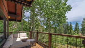 Une terrasse en bois, agrémentée d’un canapé et d’une table, entourée d’une rambarde en métal, et offrant une vue sur une zone boisée.