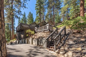 A cabin with a stone staircase leading up to a wooden deck, surrounded by tall pine trees. - Lake View from Master Bedroom, Deck,  Hot Tub, HOA Beach Access -Scenic Solitude (Carnelian Bay)