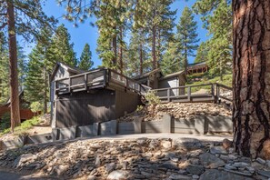 A cabin with a wooden deck and stairs leading to a balcony, surrounded by tall pine trees. - Lake View from Master Bedroom, Deck,  Hot Tub, HOA Beach Access -Scenic Solitude (Carnelian Bay)