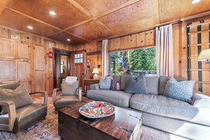 A cozy living room with wooden paneling, a sofa, armchairs, and a coffee table with a decorative plate. - Lake View from Master Bedroom, Deck,  Hot Tub, HOA Beach Access -Scenic Solitude (Carnelian Bay)