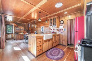 A cabin interior with a wooden interior, a kitchen area with a sink and cabinets, a dining area with a table and chairs, and a staircase leading to an upper level.